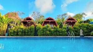 Una piscina con tre edifici a tetti rossi sullo sfondo, immersa nel verde.
