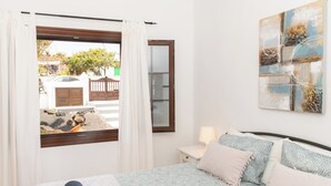 Ein Schlafzimmer mit einem Bett, einem Nachttisch, einer Lampe, einem Fenster mit Vorhängen und einem Bild an der Wand.