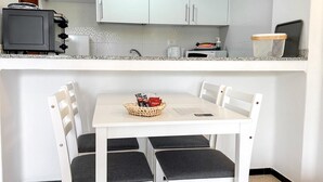 Eine kleine Küche mit weißen Schränken, einem weißen Esstisch mit vier Stühlen und einer kleinen Arbeitsplatte mit Wasserkocher und Toaster.