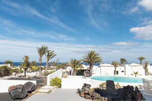 A pool area with white buildings, palm trees, and a clear sky. - Charco del Palo Fkk, Lanzarote, Villa Blanca, Apartment 3 (Charco del Palo)