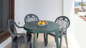 Ein überdachter Patio-Bereich mit einem runden Tisch und vier Stühlen, eine Obstschale auf dem Tisch und Blick auf den Ozean.