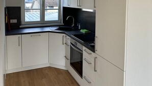 Una cocina moderna con armarios blancos, encimera negra y ventana con vistas a edificios y zonas verdes.