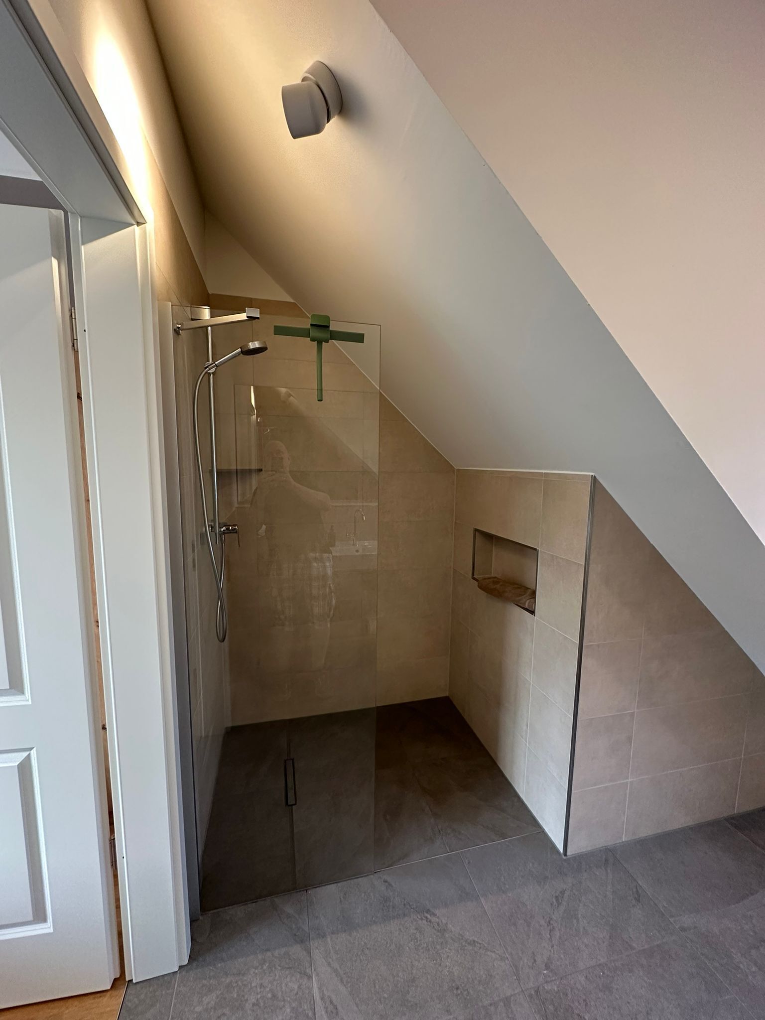 A modern shower area with a glass door, a towel rack, and a small shelf.
