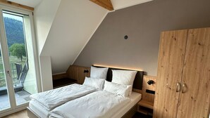 Un dormitorio moderno con una cama grande, vigas de madera en el techo, un armario y vistas a un paisaje montañoso a través de un ventanal.