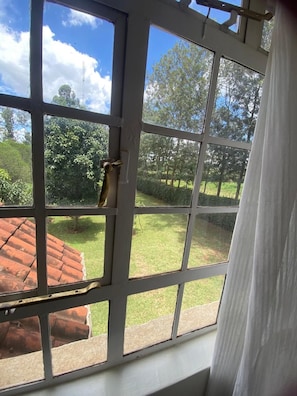 A window with a view of a garden and a red-roofed building. - Sungura Farm House (Nairobi)