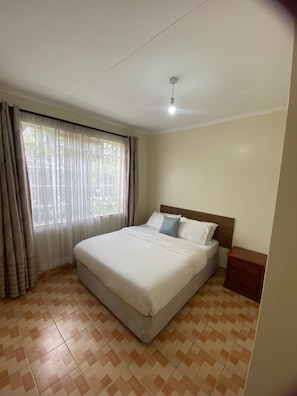 Quarto de hotel com cama, cortinas, luminária no teto e piso ladrilhado.