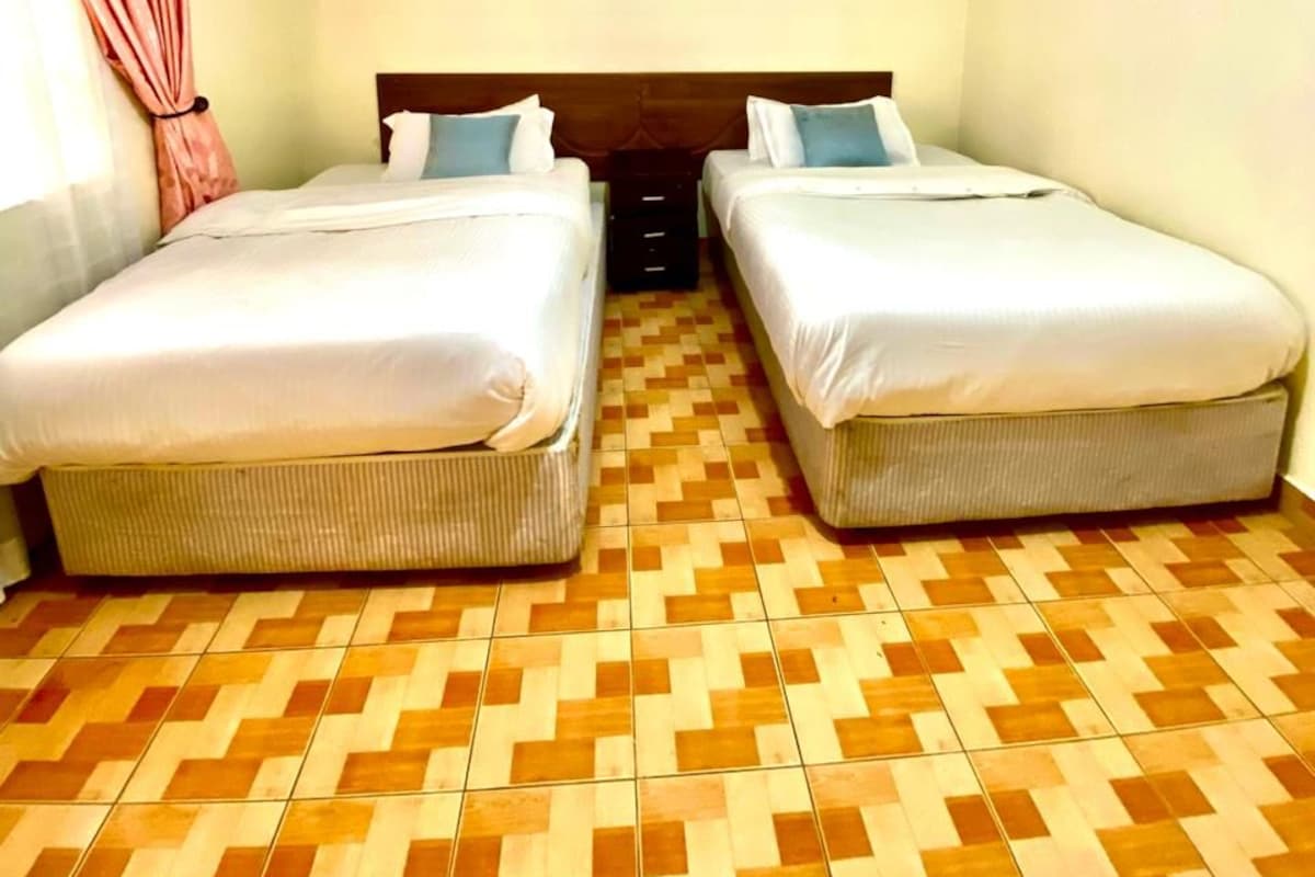 Quarto com duas camas, piso estampado e luminária no teto.