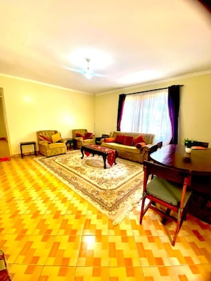 Uma sala de estar com sofá, poltronas, mesa de centro e mesa de jantar.