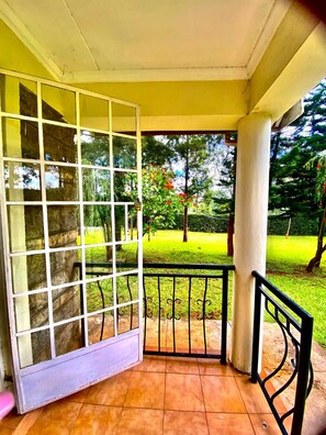 A covered outdoor area with a glass door leading to a garden. - Sungura Farm House (Nairobi)