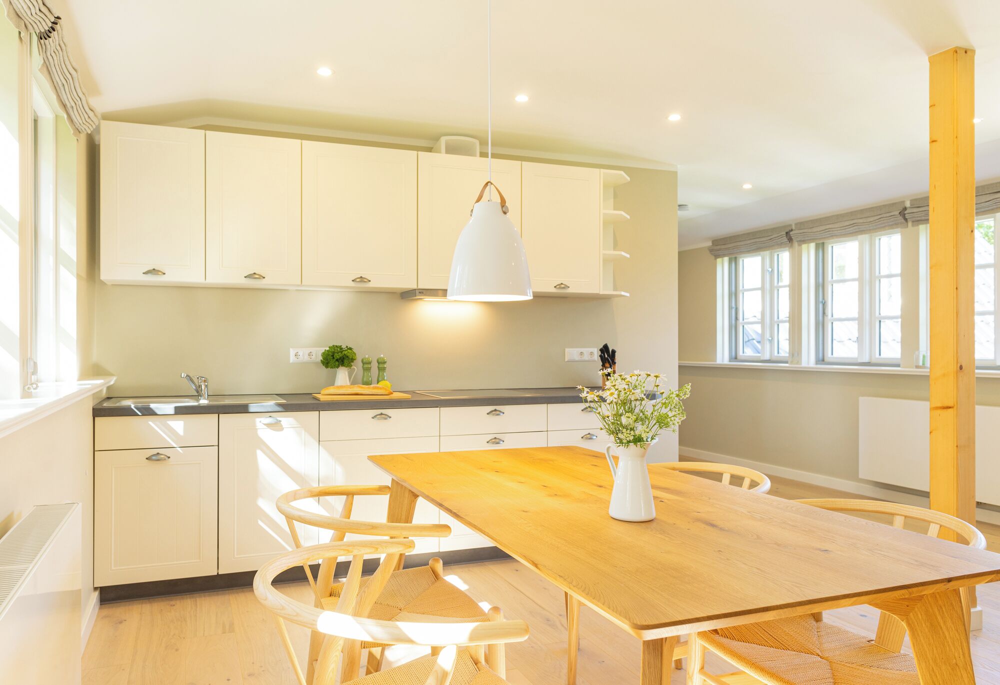 A modern kitchen with white cabinets, a wooden dining table, and a hanging pendant light.