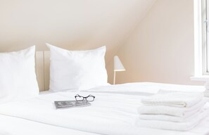 Ein ordentlich bezogenes Bett mit weißen Laken, eine Brille und ein Buch darauf.