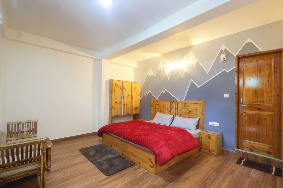 A bedroom with a wooden bed, a red blanket, a wooden wardrobe, and a bench.