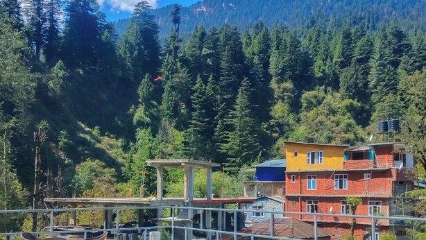 Una terraza con sillas de plástico, una construcción de concreto y vista a una montaña boscosa.