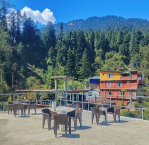 Una terraza con sillas de plástico, una construcción de concreto y vista a una montaña boscosa.