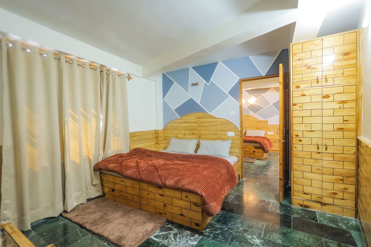 A bedroom with a wooden headboard bed, a wooden wardrobe, and a geometric-patterned wall.