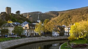 Un pueblo histórico con un puente de piedra, edificios y una iglesia en una colina.