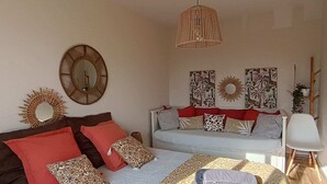 Una sala de estar acogedora con sofá, sillón y cama. Se observan espejos decorativos y obras de arte en las paredes.