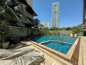 A swimming pool with a tiled deck, surrounded by palm trees and a stone wall. - The ClubHouse Residence by PSR (Pattaya)