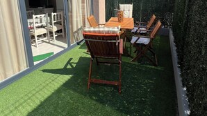 Un patio con tavolo e sedie, una porta scorrevole in vetro che dà su un ambiente interno e un siepe lungo il lato.