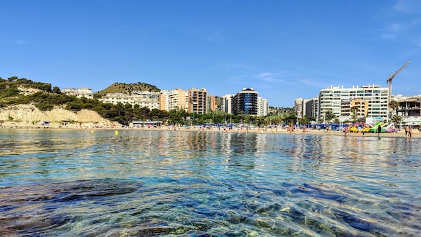 A coastal cityscape with clear waters reflecting buildings, a sandy beach, and a hilly backdrop. - CALA ALTA design apartment (Benidorm)