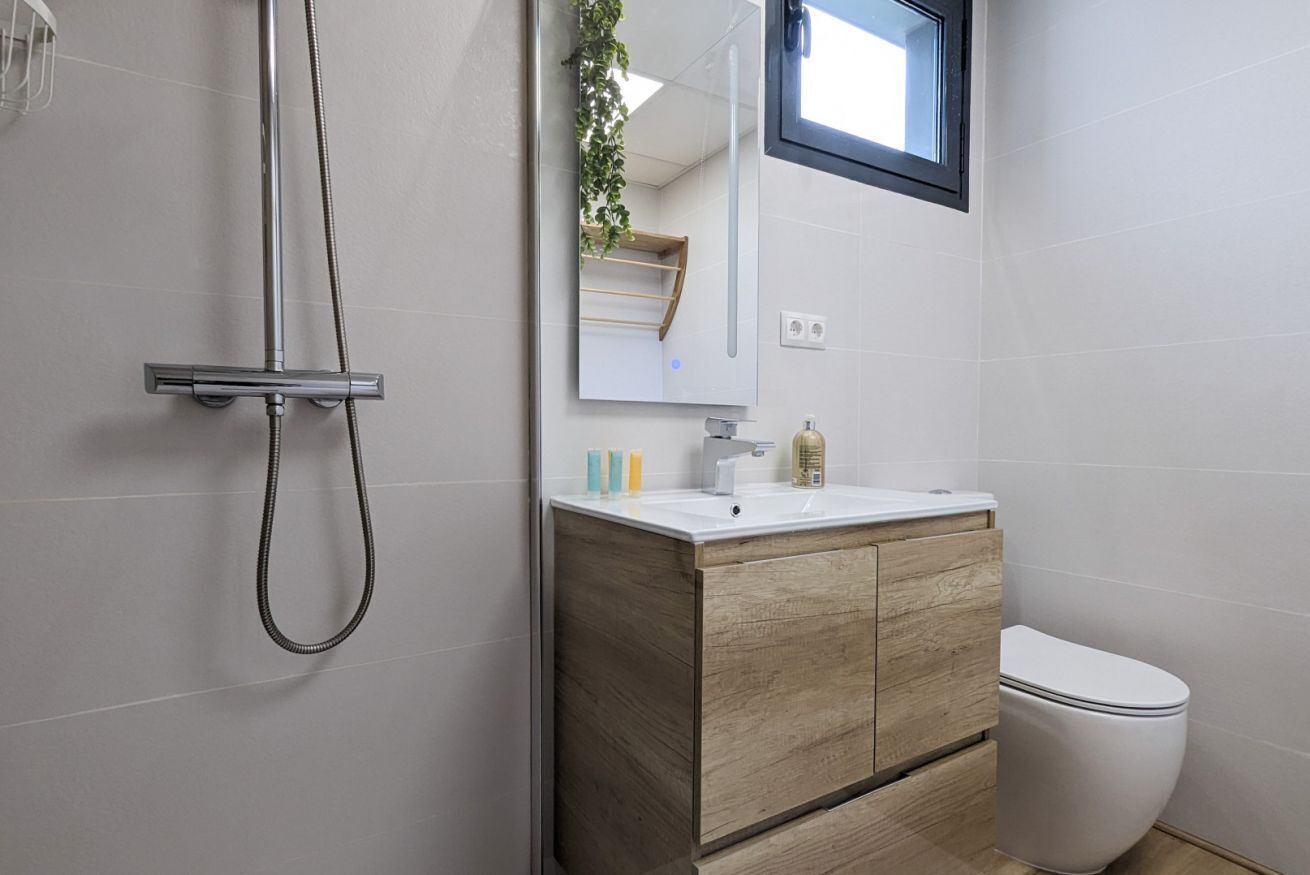 Une salle de bain moderne avec une douche, un lavabo doté d’un meuble en bois, des toilettes et un miroir agrémenté d’une plante.
