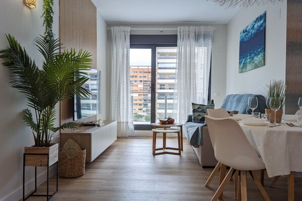 A modern living room with a dining area, large windows, and a view of the city.