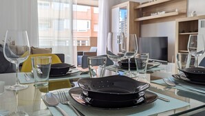 Un coin repas avec une table en verre mise pour quatre personnes, comprenant des assiettes, des couverts et des verres à vin.