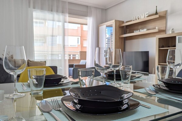 A dining area with a glass table set for four, including plates, cutlery, and wine glasses.