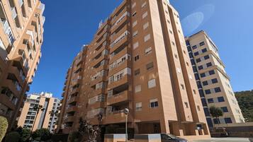 Un edificio residencial de varios pisos con balcones, un estacionamiento y cielo despejado.