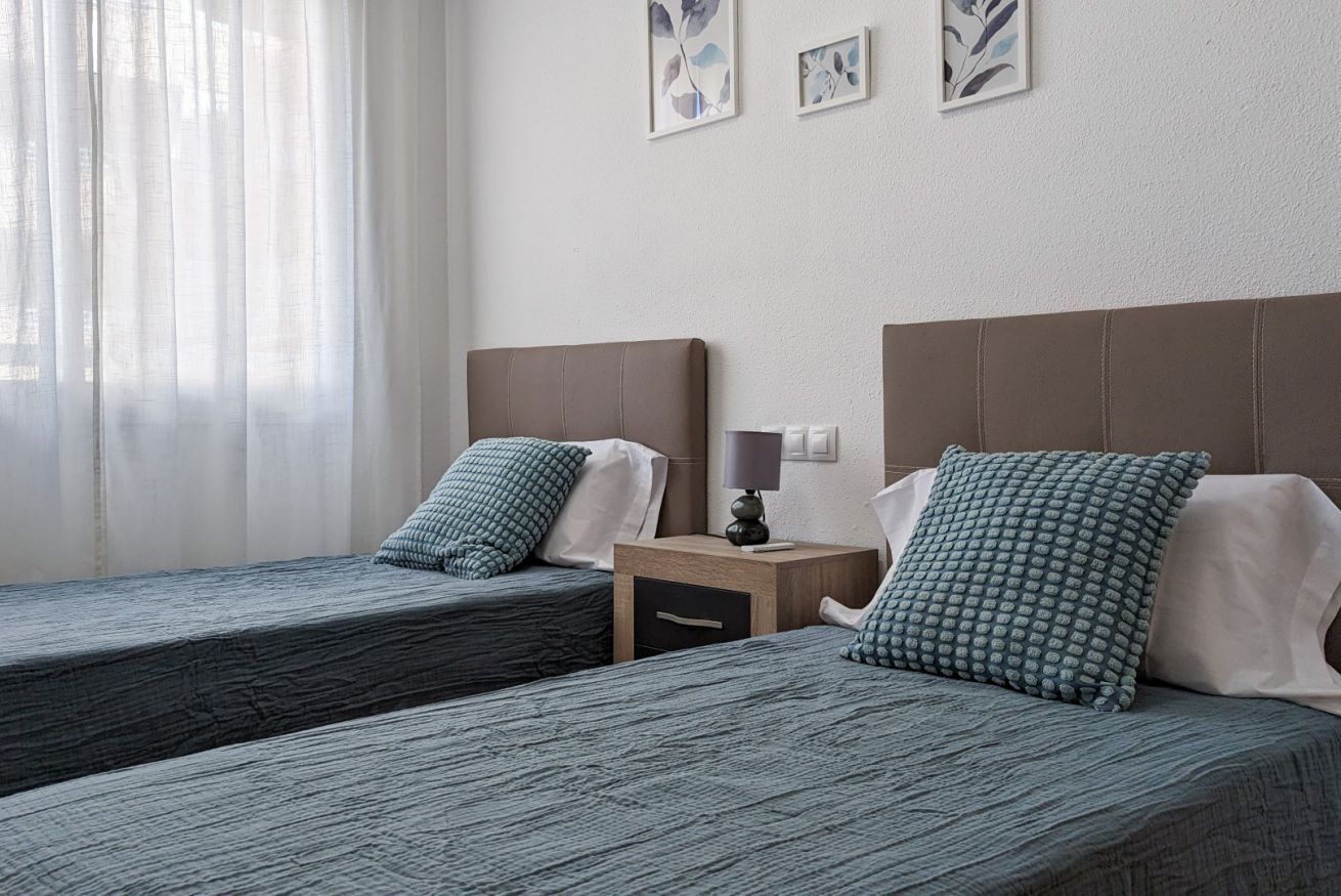 Una habitación de hotel con dos camas individuales, cada una con una almohada y una mesita de noche con lámpara.