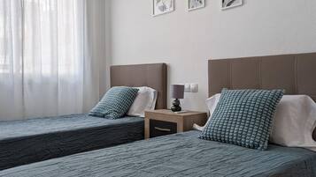 Una habitación de hotel con dos camas individuales, cada una con una almohada y una mesita de noche con lámpara.