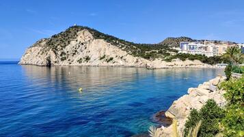 Un paisaje costero con aguas azules cristalinas, costa rocosa y edificios al fondo.