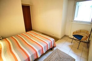 Ein kleines, ordentlich eingerichtetes Schlafzimmer mit einem Bett, einem Sessel und einem Fenster.