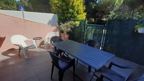 Eine Terrasse mit Tisch und Stühlen, einem kleinen runden Tisch und Blumentöpfen.