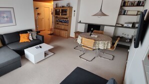 A living room with a grey sofa, a white coffee table, and a dining area with a round table and chairs. - Gemütliches Appartement für Erholung und Sport (Klosters-Serneus)