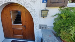 A wooden door with a glass panel, a stone wall, a potted plant, and a keypad lock. - Gemütliches Appartement für Erholung und Sport (Klosters-Serneus)