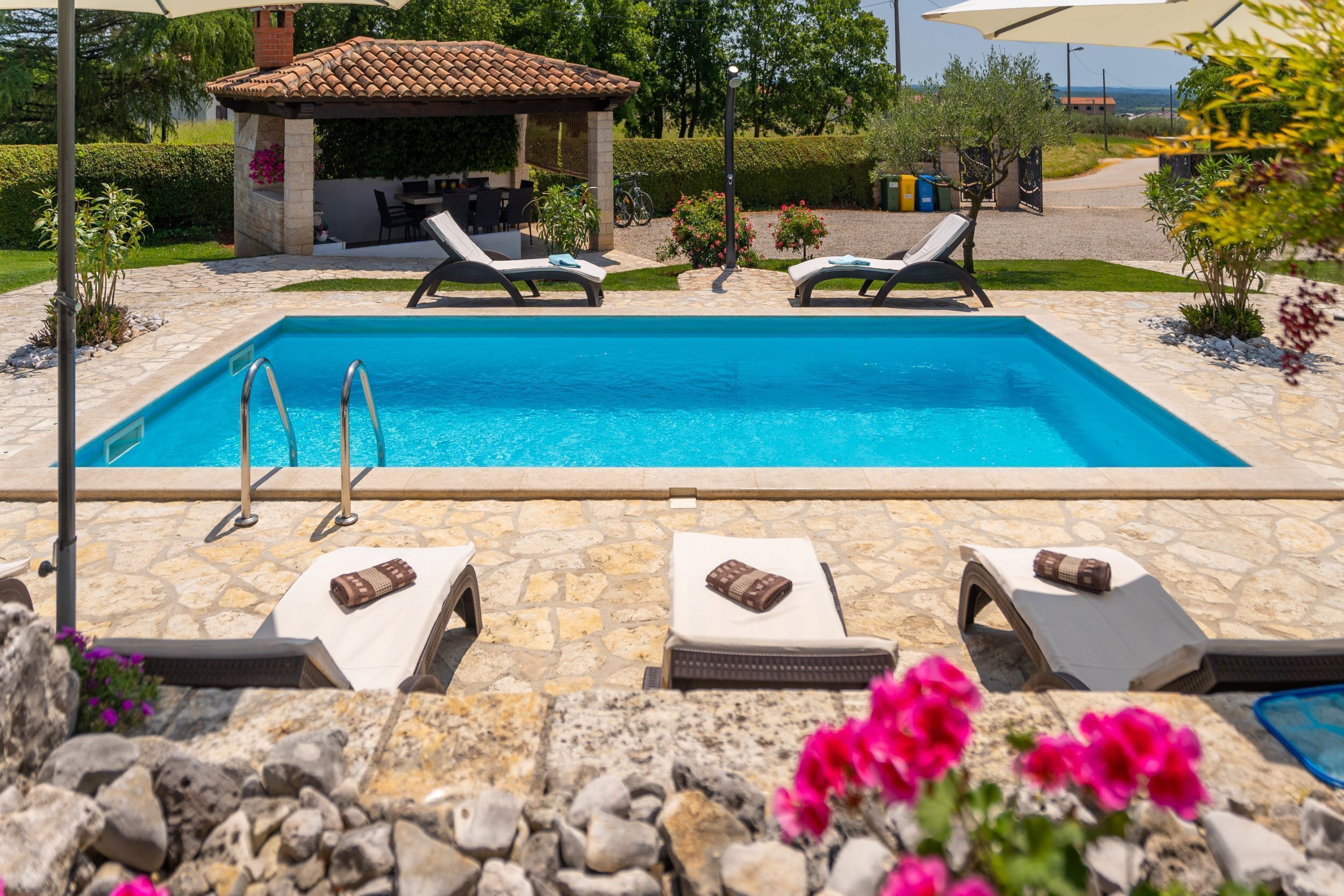 A rectangular swimming pool with two lounge chairs and a small covered seating area in the background.