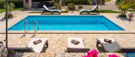 A rectangular swimming pool with two lounge chairs and a small covered seating area in the background.