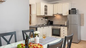 Een moderne keuken met witte kasten, een roestvrijstalen koelkast en een eettafel gedekt met een fruitschaal en wijn.