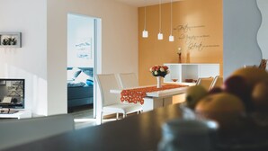 A modern living room with a dining area, featuring a sofa, chairs, a table with a vase of flowers, and a wall with a decorative quote.