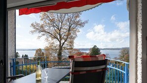 A balcony with a table and chairs, overlooking a lake and trees.