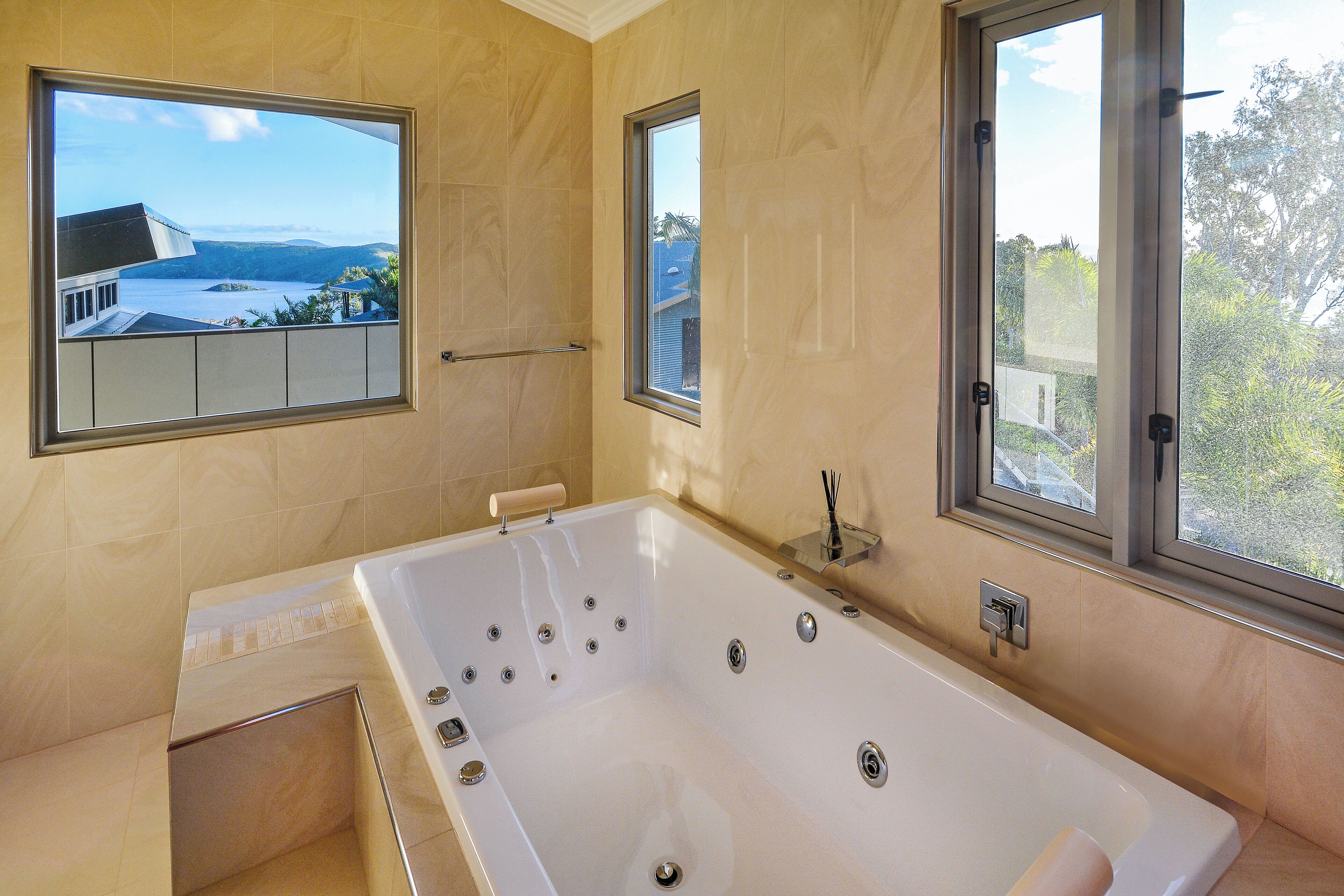 A modern bathroom with a large bathtub, two windows with views of a landscape, and a shower area.
