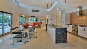 A modern kitchen with a central island, stainless steel appliances, and a glass-top dining table with chairs. - Jasmine house  (Hamilton Island)