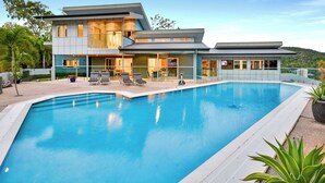 A modern two-story house with a swimming pool, outdoor seating, and a view of a hilly landscape. - Jasmine house  (Hamilton Island)
