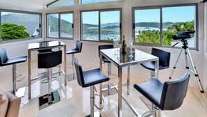 A modern dining area with high ceilings, large windows, and a view of the sea. - Jasmine house  (Hamilton Island)
