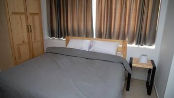 A bedroom with a bed, curtains, a wardrobe, and a bedside table with a lamp.