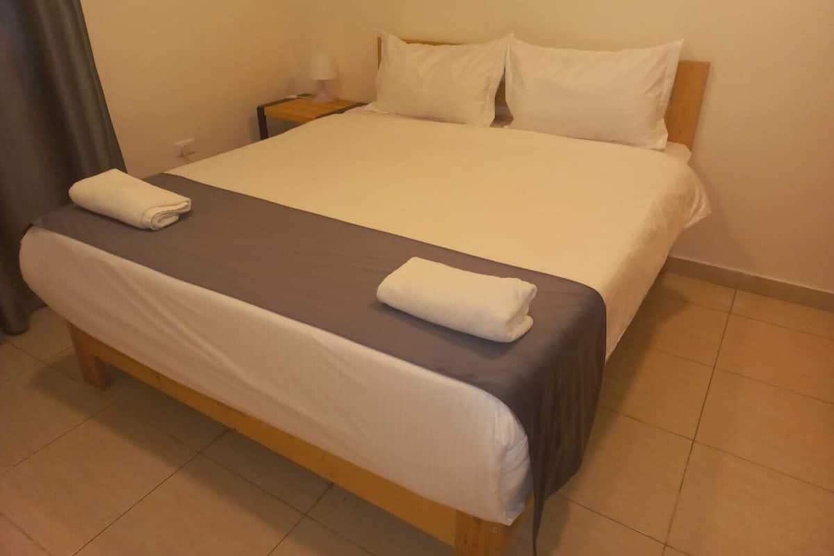 A neatly made bed with white linens and two towels folded on the bed.