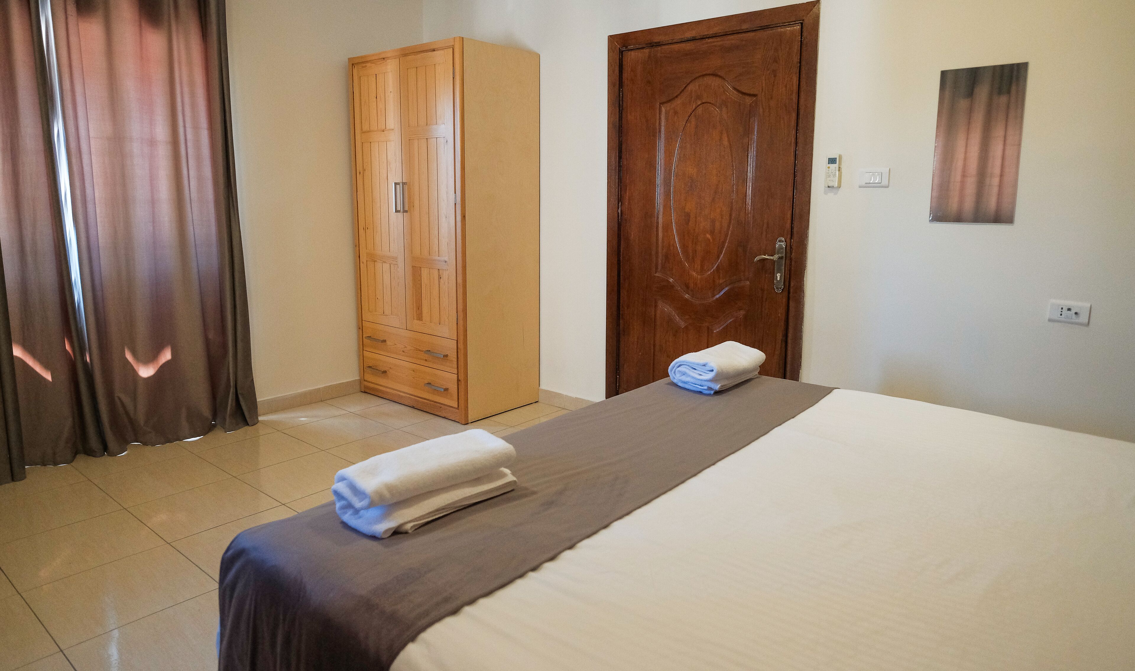 A hotel room with a bed, a wardrobe, a door, and a wall-mounted light switch.
