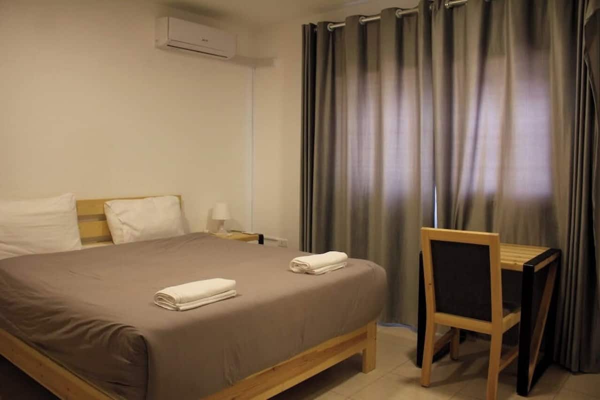 A hotel room with a bed, a chair, a nightstand, and a window with curtains.