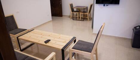 A room with a wooden bed frame, two chairs, a small table, a TV, and a door.